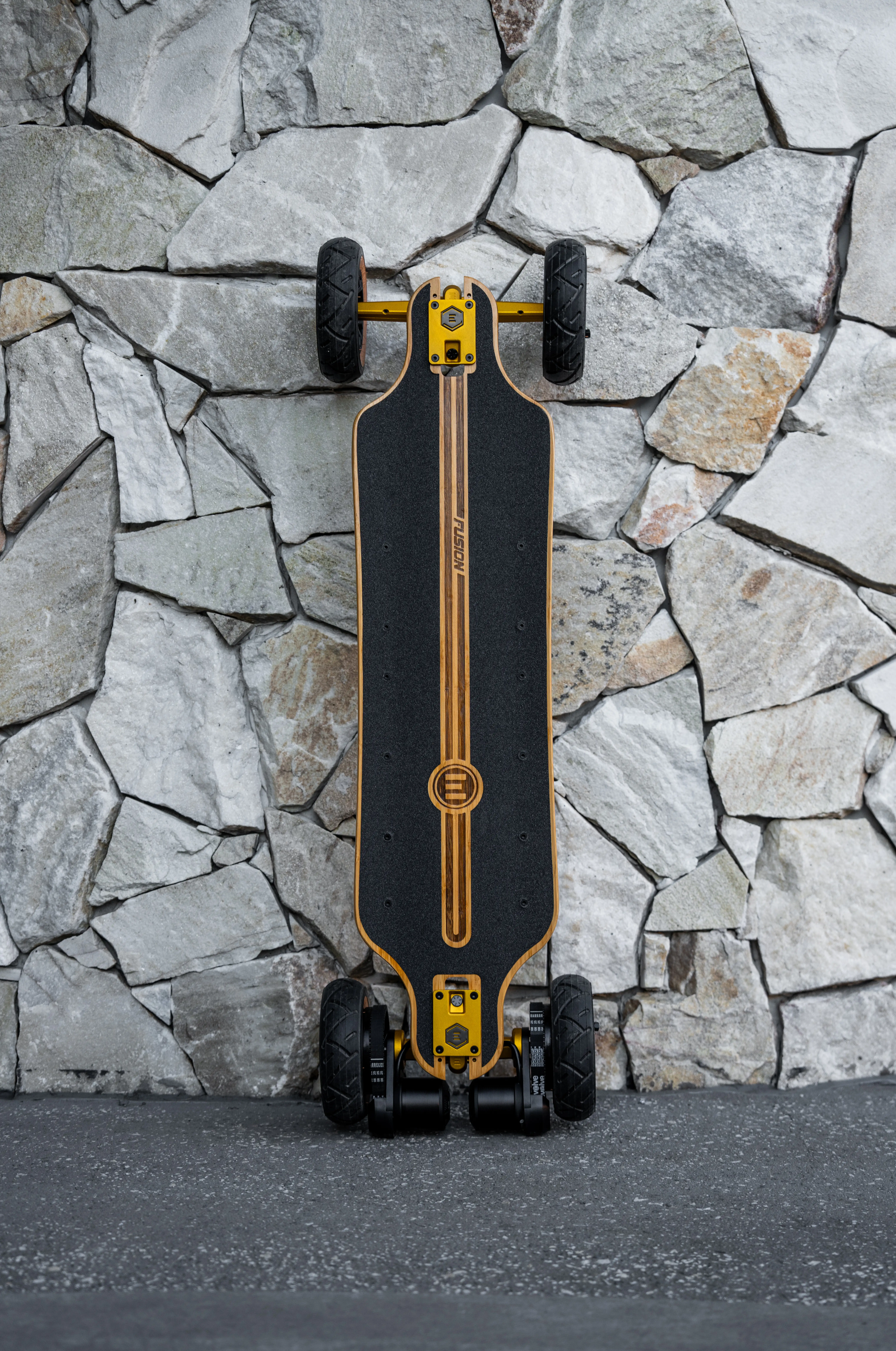 Photo du e-skate fusion posé à la verticale sur un mur en pierres